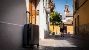 Une valise posée contre un mur blanc dans une ruelle de Séville, tandis qu'un voyageur au sac léger s'éloigne pour visiter la ville